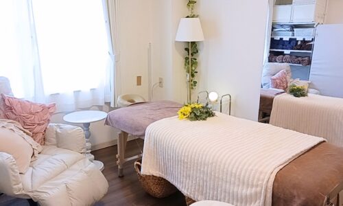 白いレースカーテン越しに自然光が差し込む室内に、施術ベッドとリクライニングチェアが配置された明るい空