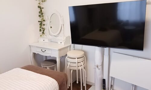 白いドレッサーと椅子、スタッキングスツール、壁掛けテレビモニター、折りたたみテーブルが並ぶサロン設備