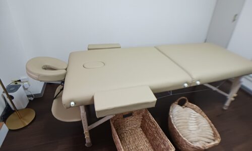 リクライニング可能なベージュ色のマッサージベッドと、足元に置かれた2つの収納バスケット
