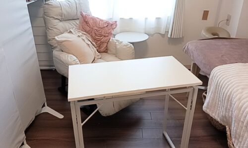 リクライニングソファの前に折りたたみ式の白いテーブルが置かれ、施術ベッドも隣接している明るい施術スペース