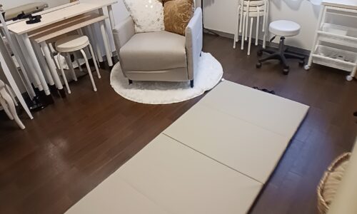 施術用の折りたたみマットが床に敷かれ、奥にはクッションが置かれたチェアと作業台があるレンタルサロンの一角