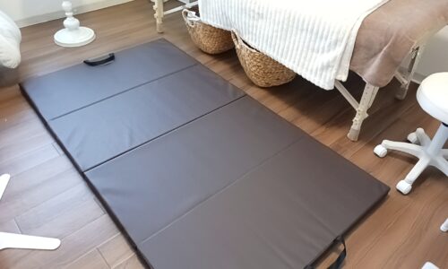 ブラウンの折りたたみ式床マットが施術ベッドの横に広げられたサロンの一角